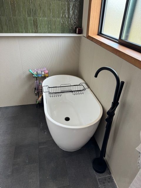 Bathroom with a white oval bathtub, black faucet, and green tile wall.