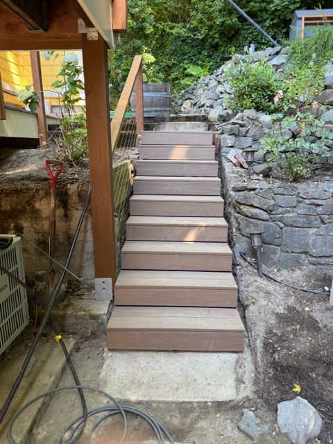 Wooden outdoor stairs leading upwards, next to a rock wall and hillside.