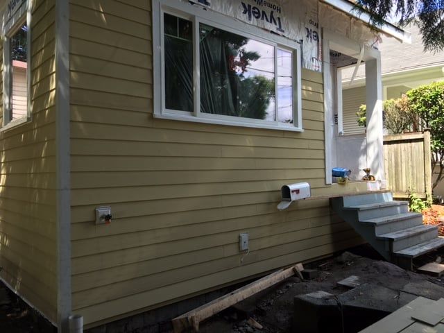 Yellow house exterior under construction, white window and trim, steps leading to the door.