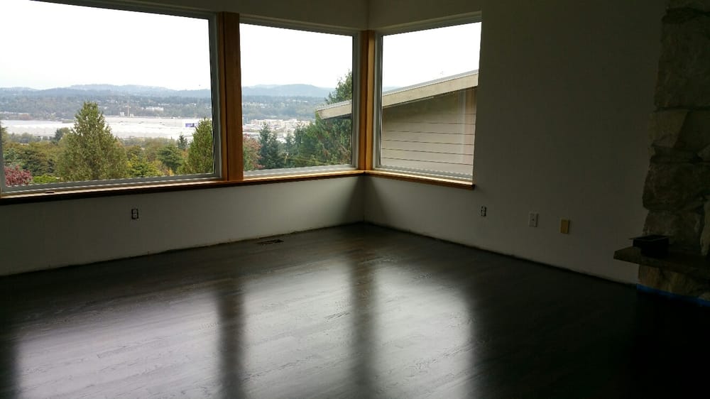 Empty room with dark wood floors, large corner windows, and a view of trees and water.