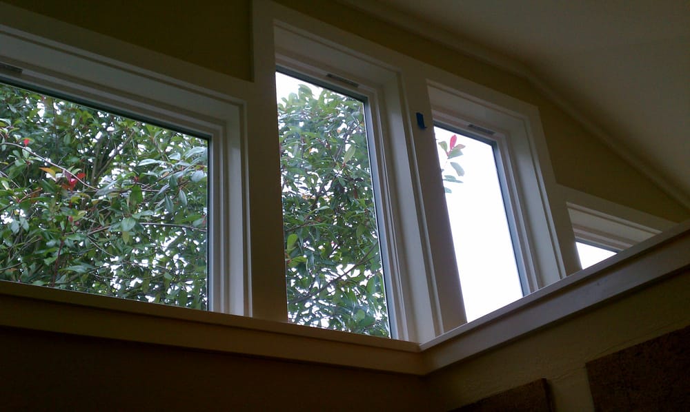 Three white framed windows in a wall, with trees visible outside.