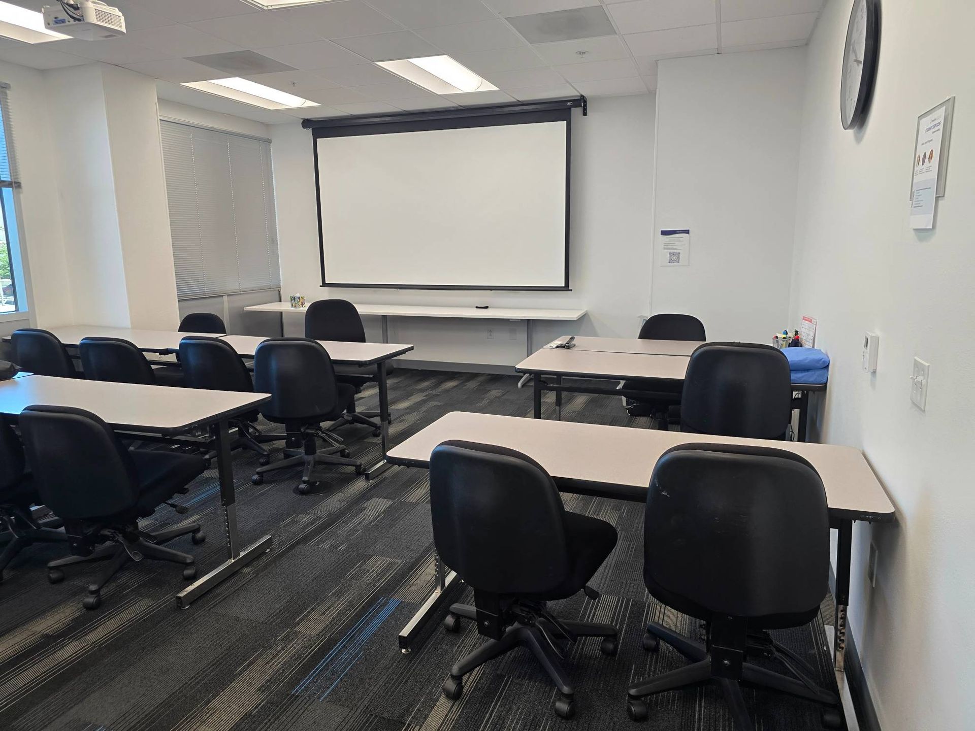 A classroom with tables and chairs and a projector screen.