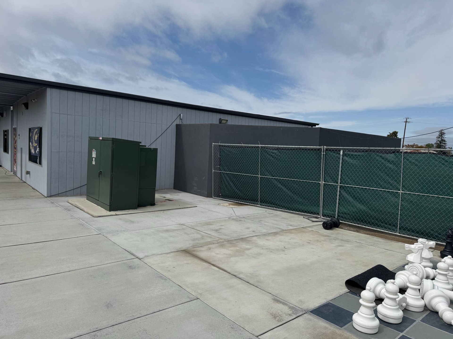 A large chess board is sitting in front of a building behind a chain link fence.