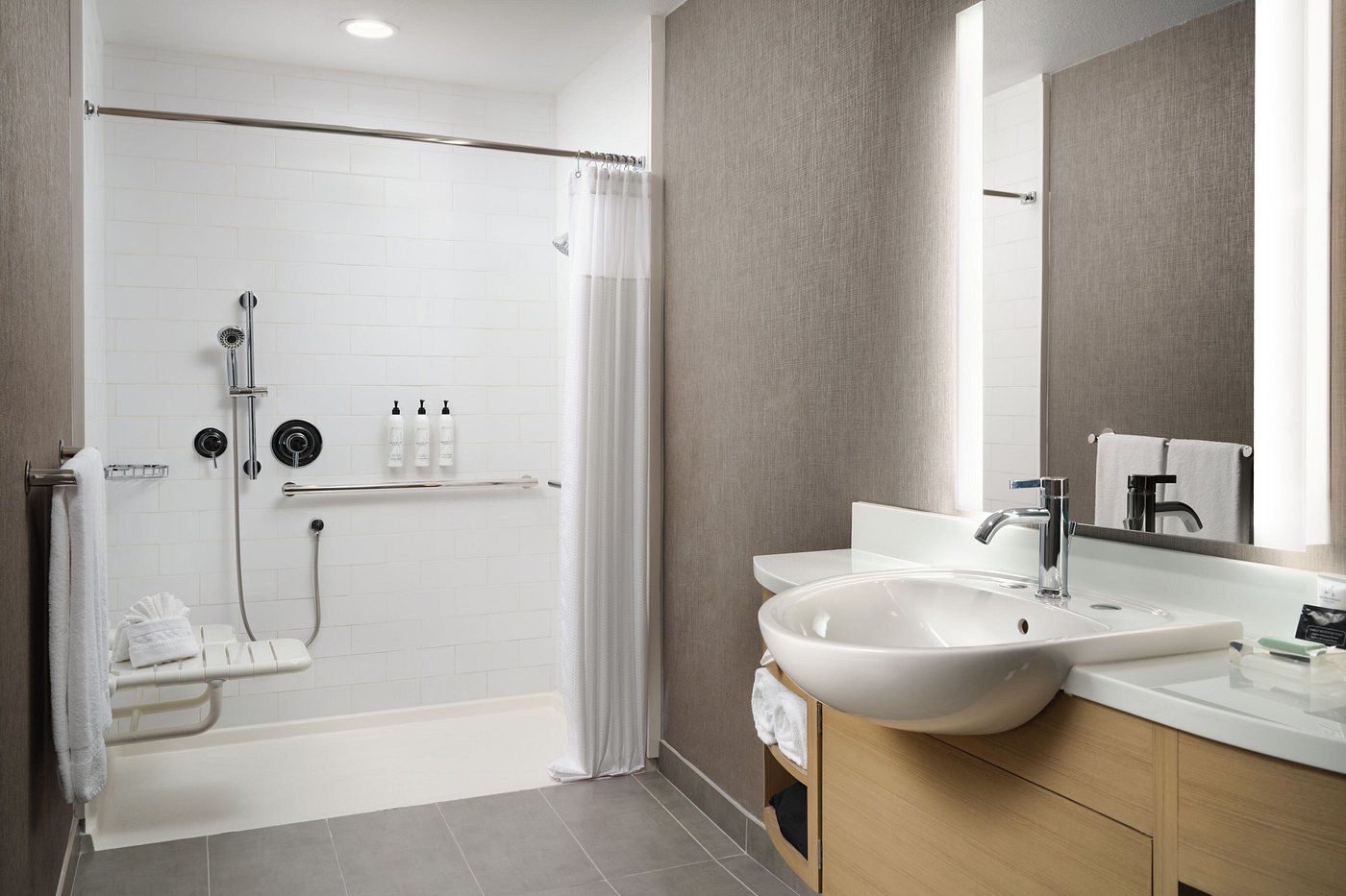 A bathroom in a hotel room with a sink , mirror and shower.