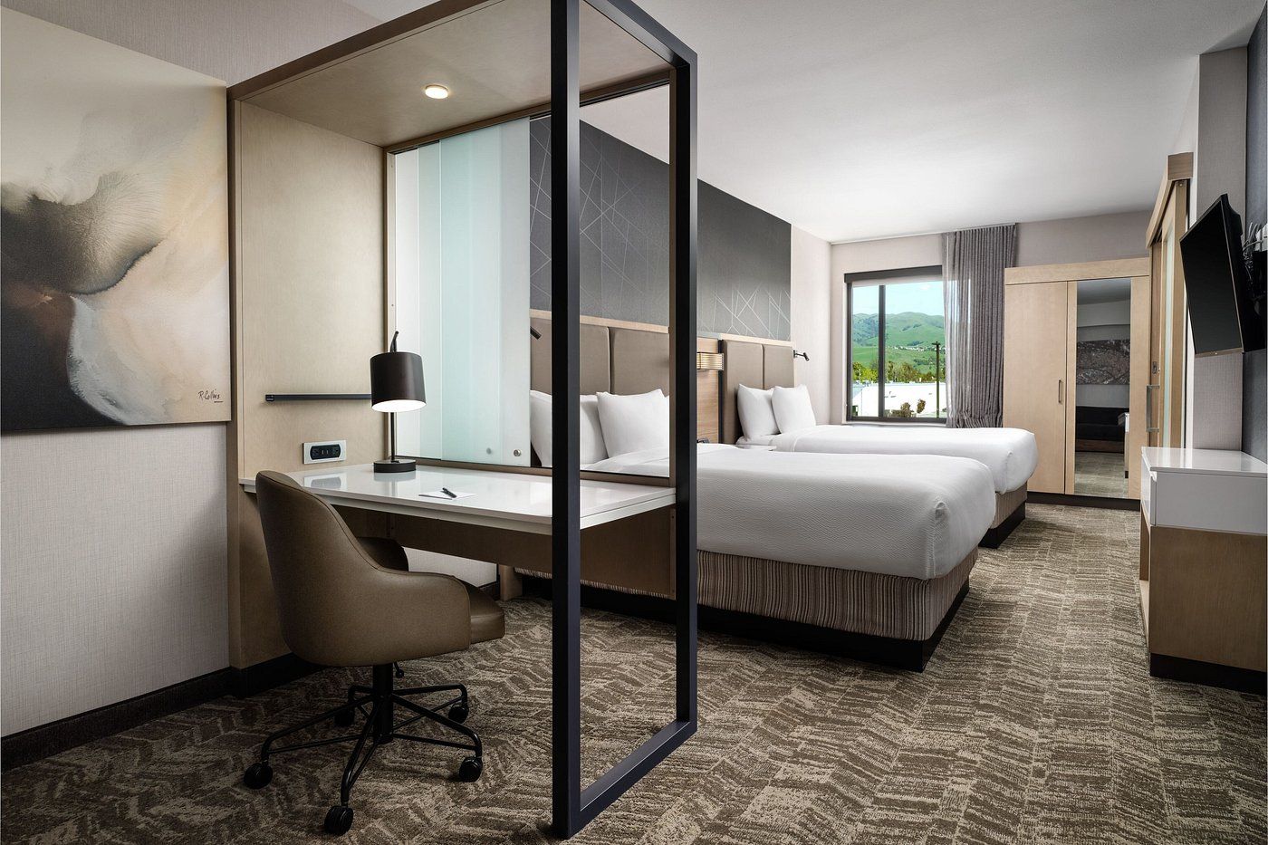 A hotel room with two beds , a desk and a chair.