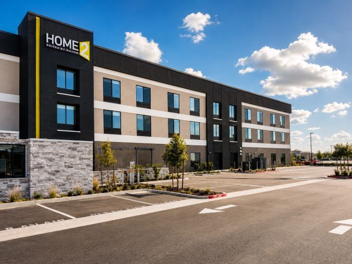 Modern three-story Home2 hotel exterior with black and beige facade under a blue sky