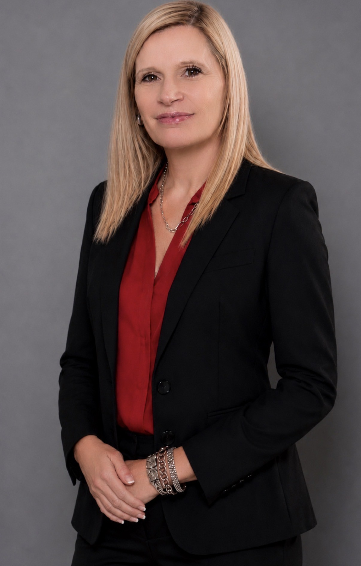 Formal portrait of a woman in a black blazer and red blouse against a gray background