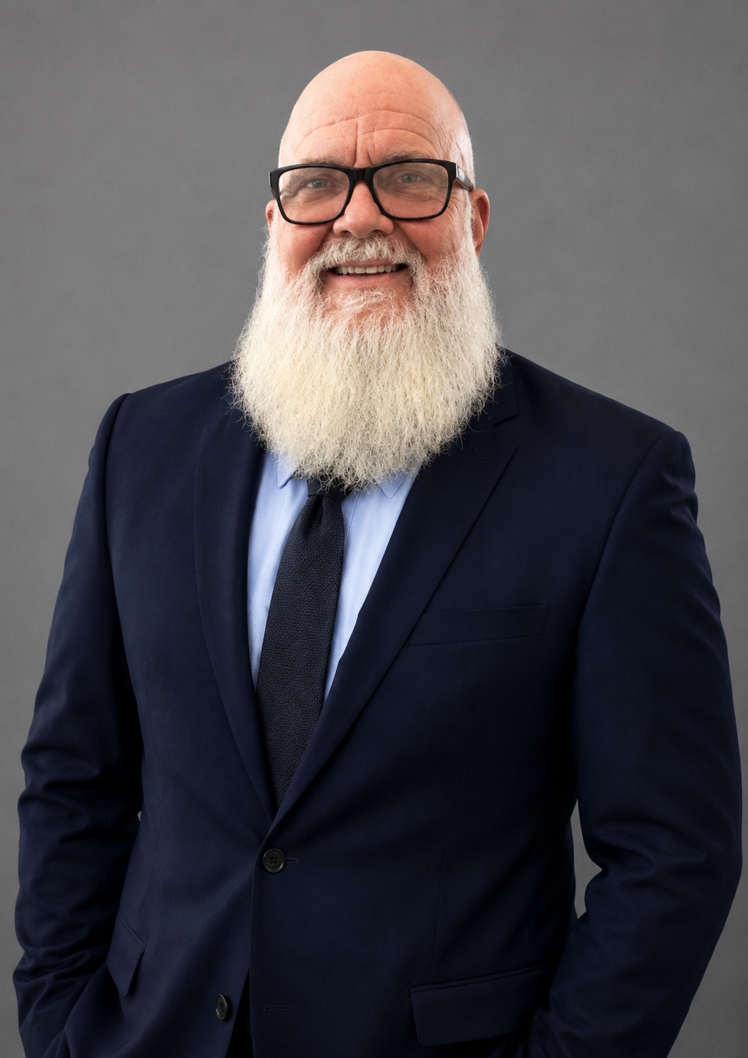 Smiling bearded man in a navy suit and tie against a gray background