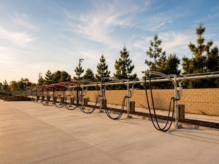 Row of bike racks beside a tan wall on a sunny sidewalk with trees in the background