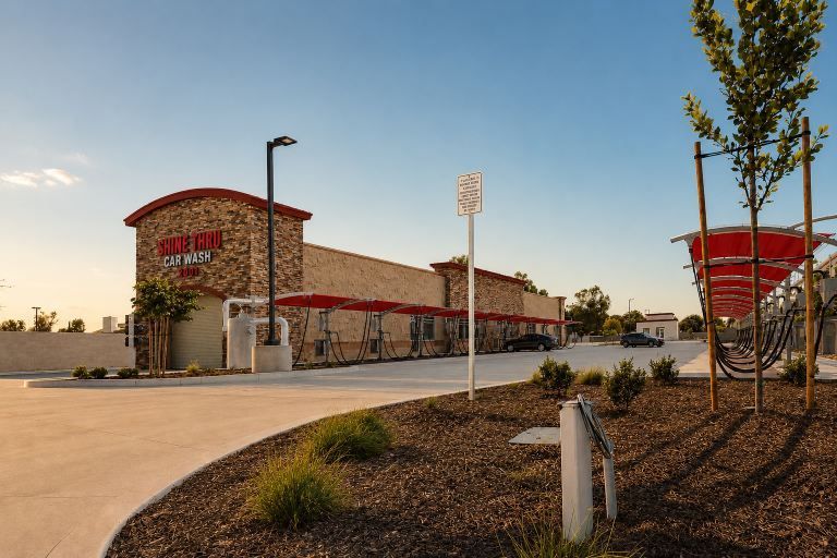 Brick store building with red accents beside a parking lot at sunset