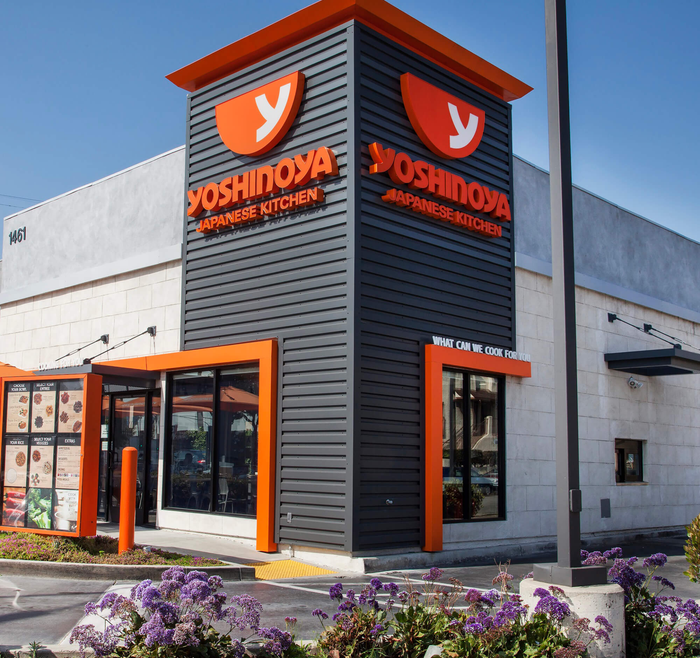 A yoshinoya restaurant with purple flowers in front of it