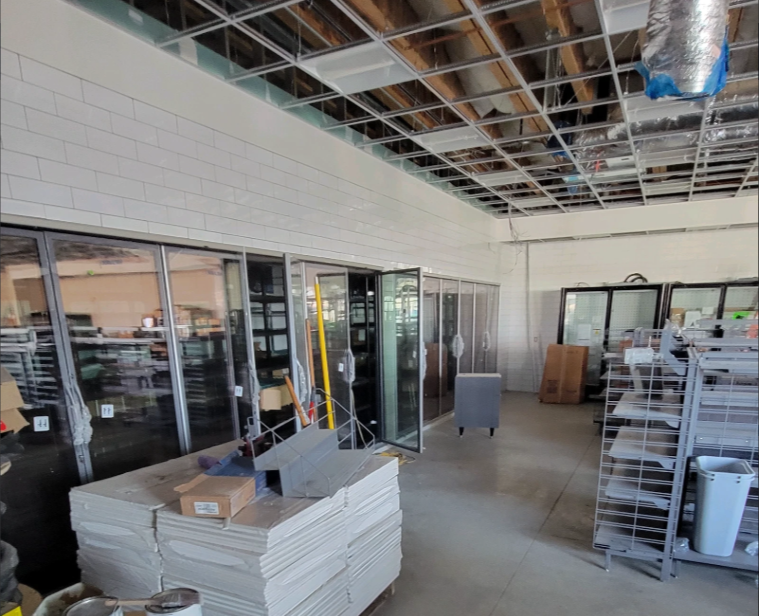 Interior under construction with glass doors, white walls, exposed ceiling grid, and construction materials.