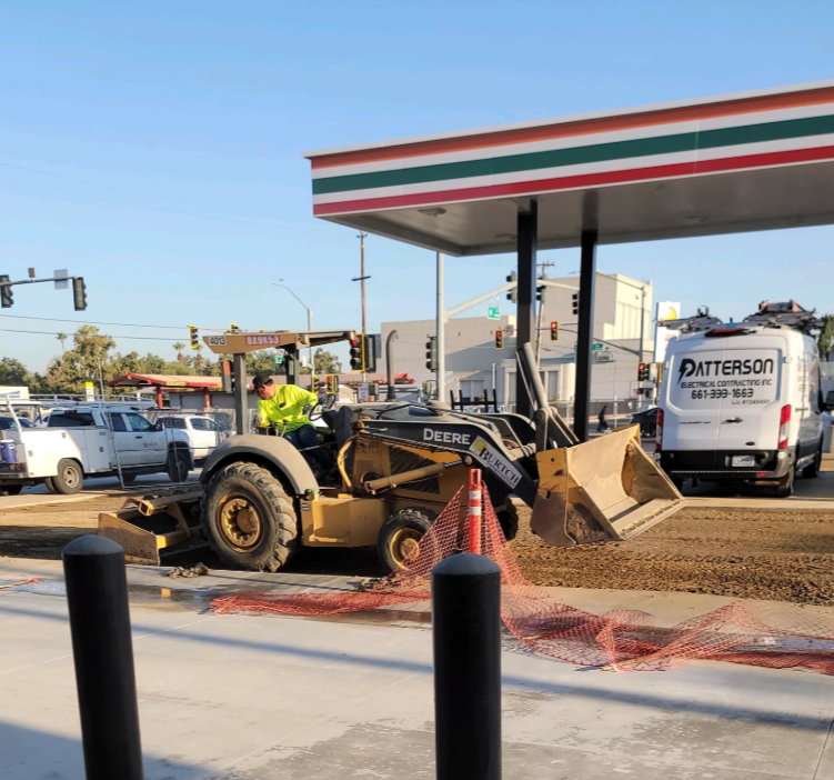 Construction site at a 7-Eleven gas station. A yellow tractor moves gravel. A white van is parked nearby.