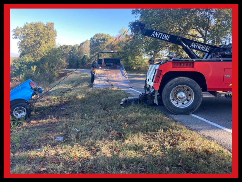 A tow truck loading a blue car on the side of a road.