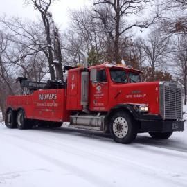 Red tow truck on a snow-covered road; a forested backdrop.