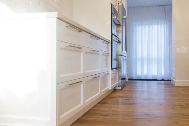 Une cuisine avec des armoires blanches, du parquet et des appareils électroménagers en acier inoxydable.