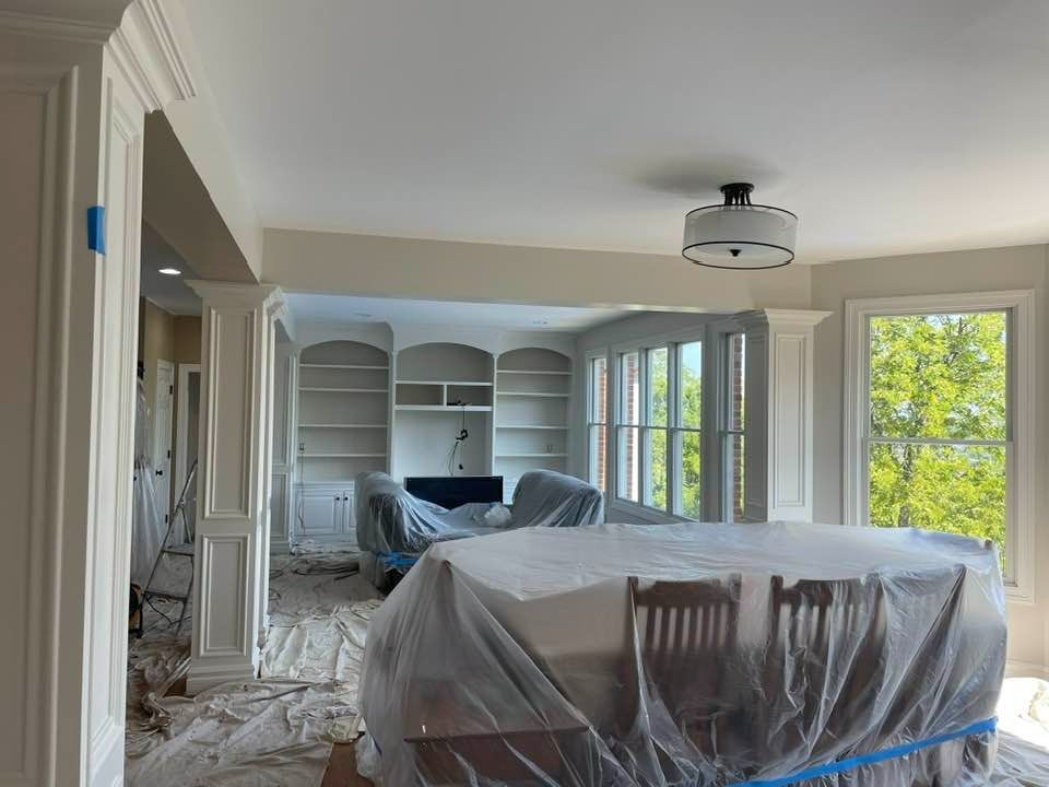 Room under renovation with covered furniture, built-in shelves, and trim work; white walls and ceiling.