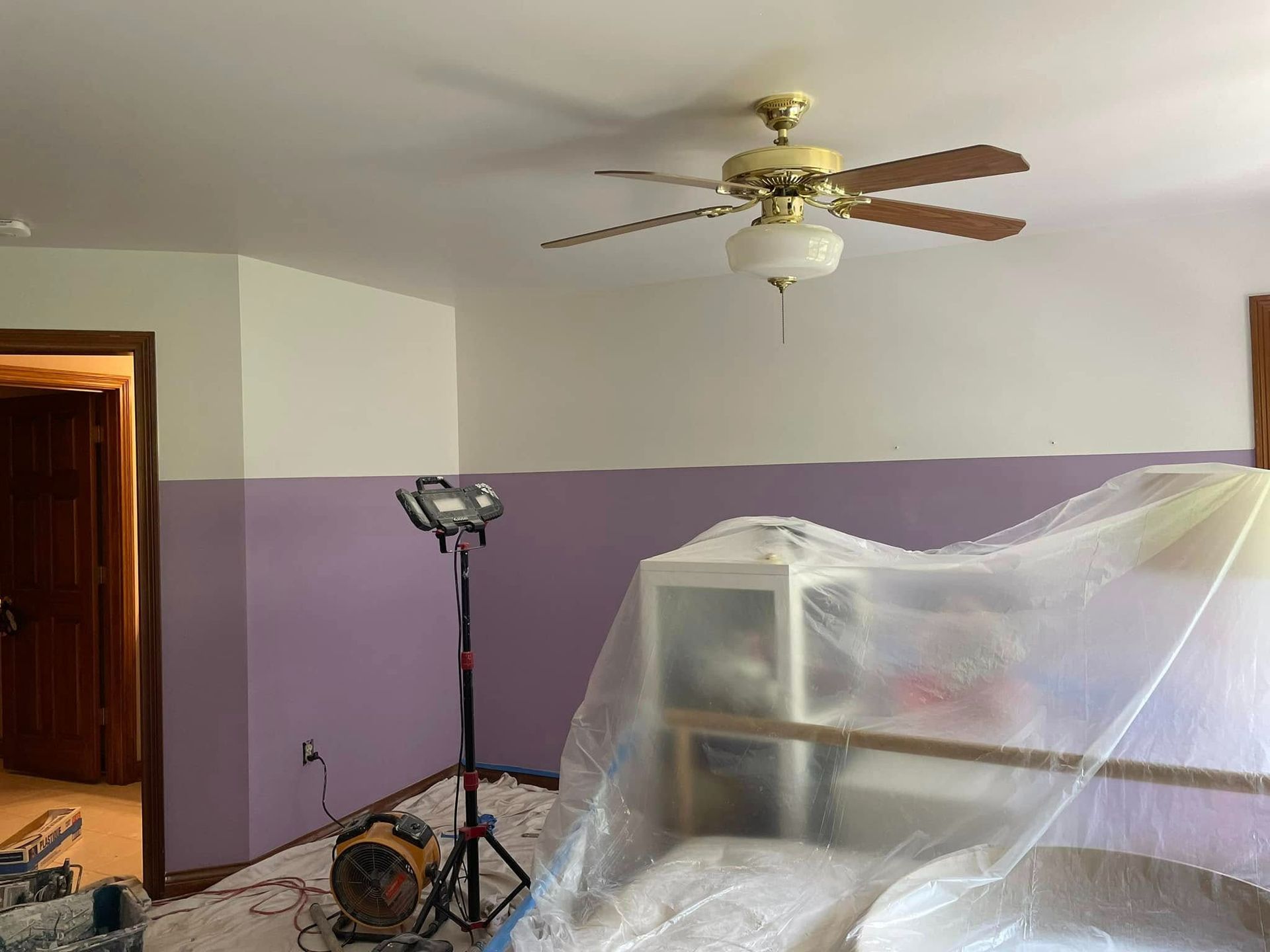 Bedroom with two-tone walls (white & purple), covered furniture, work light, and a ceiling fan.