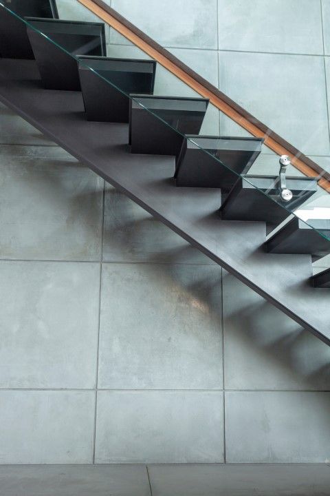Metal step staircase with glass railing alongside a tiled concrete wall