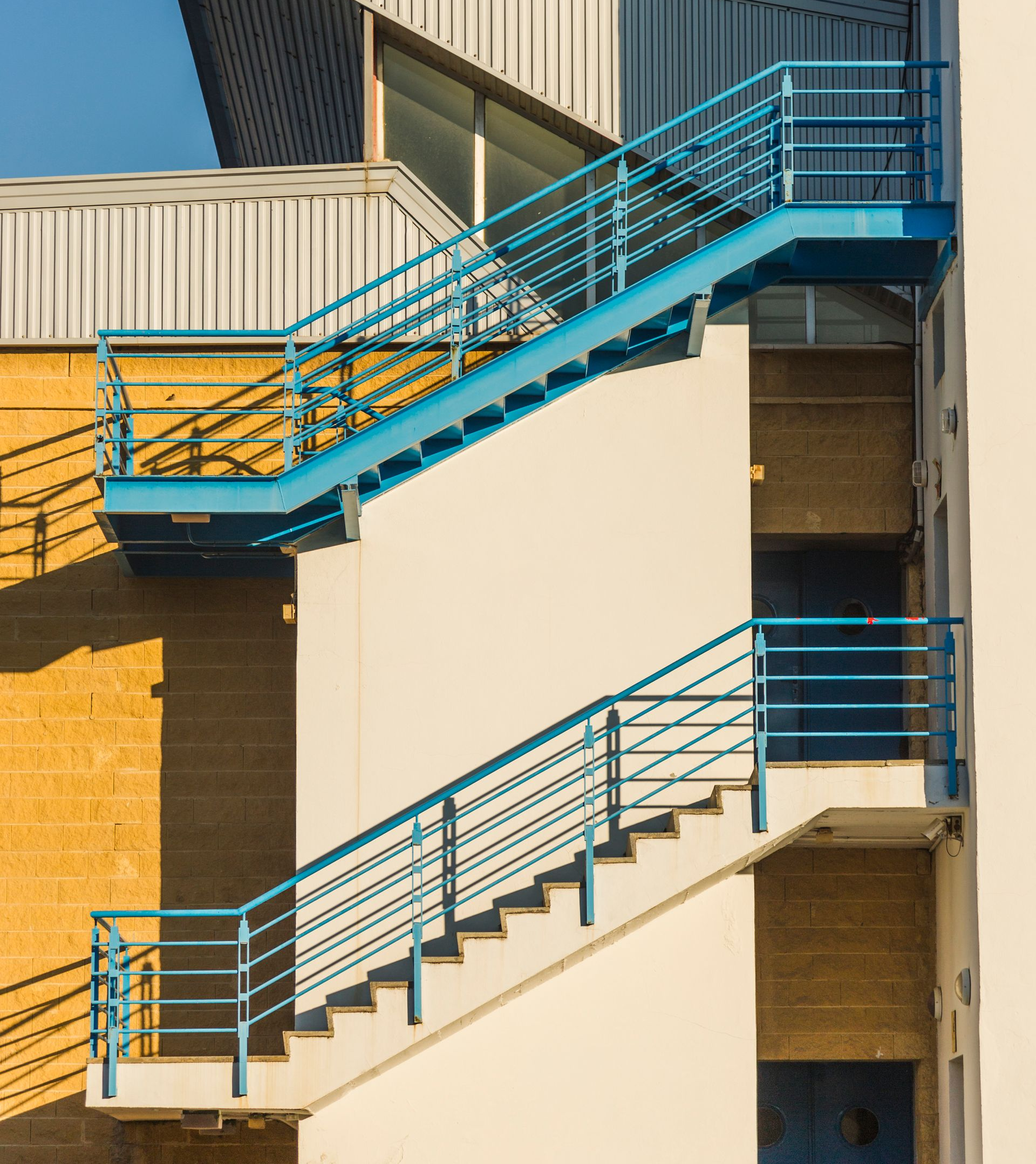 Blue outdoor metal staircases run along the side of a cream-colored exterior building