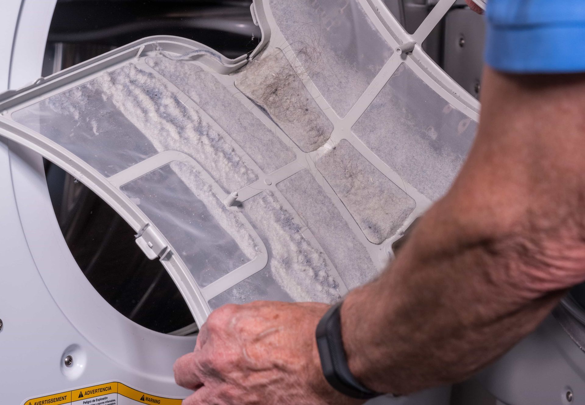 Person cleaning a lint filter from a dryer, holding a dusty mesh screen open