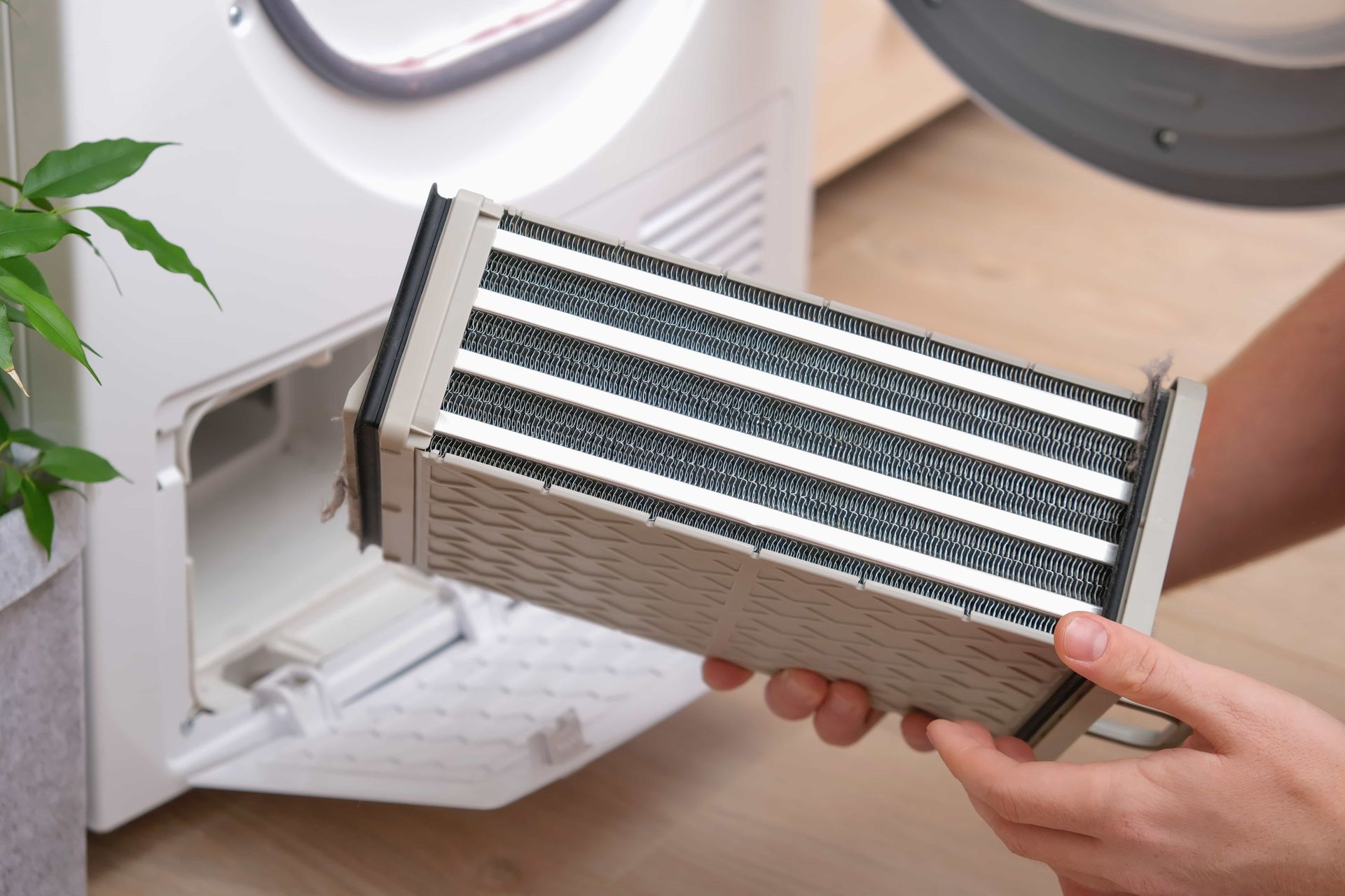 Hands holding a dirty air filter in front of an open white dryer lint compartment.