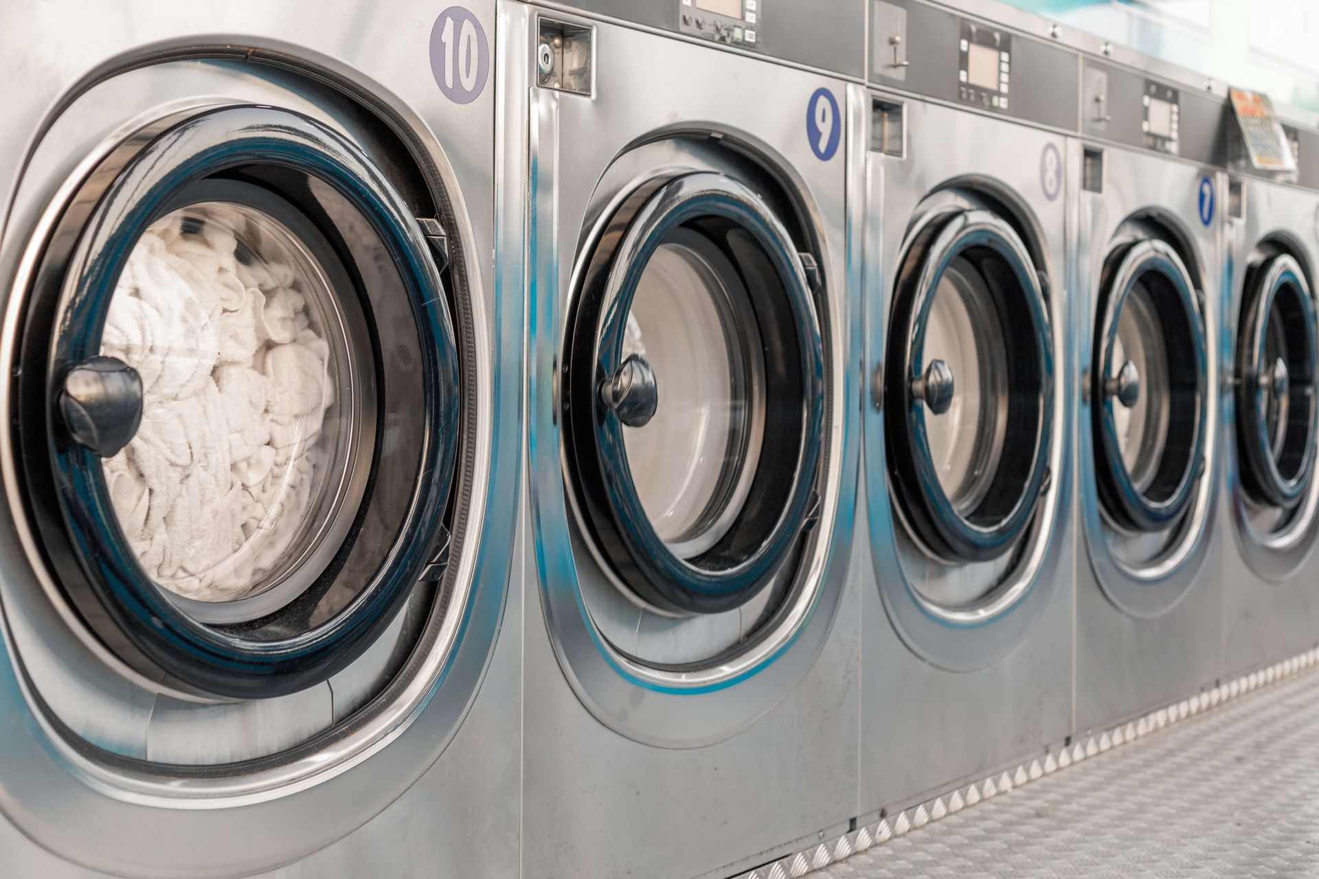 Row of stainless steel front-loading washing machines in a laundromat