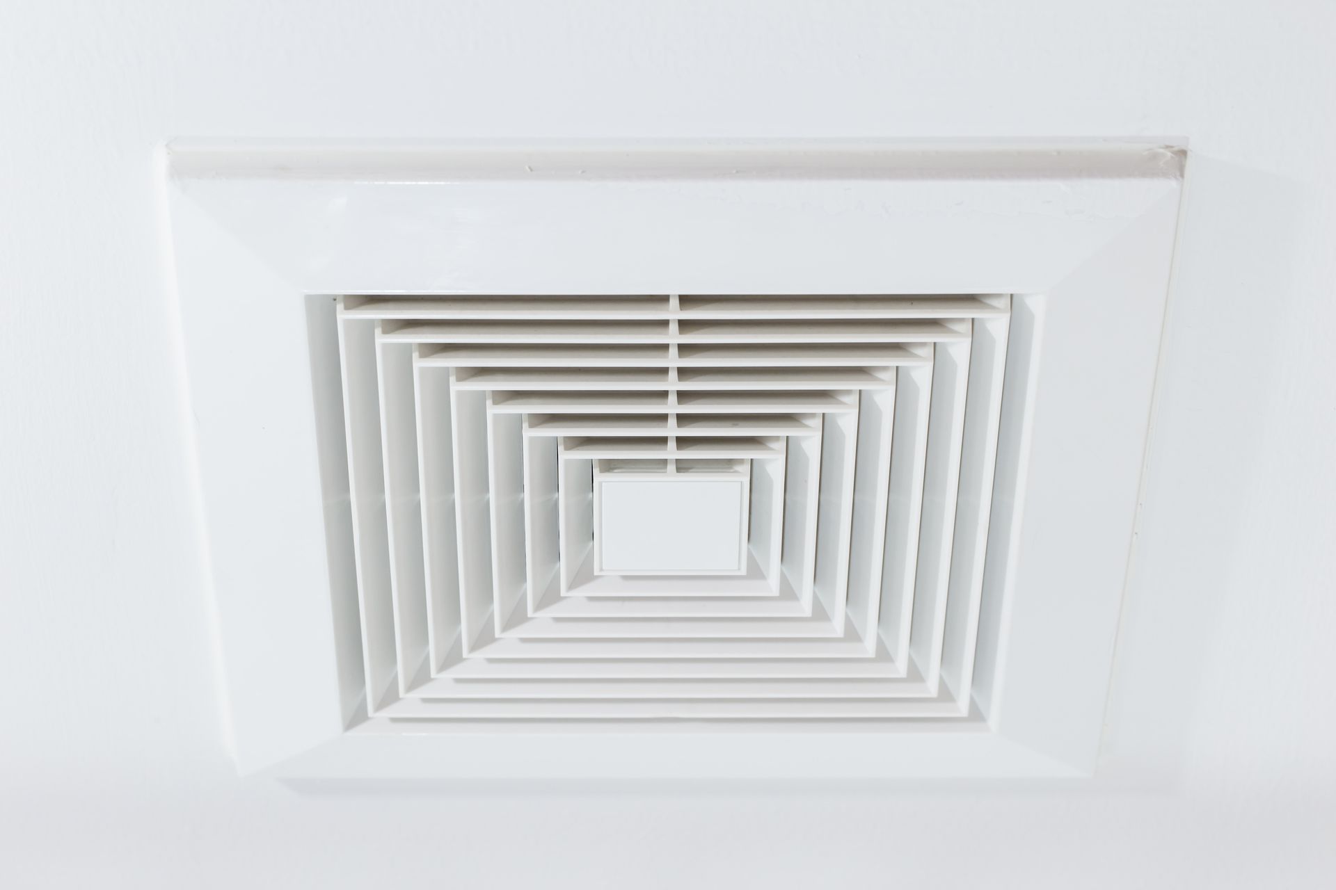 White square ceiling air vent with layered slats on a white ceiling
