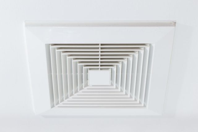 White square ceiling air vent with layered slats on a white ceiling