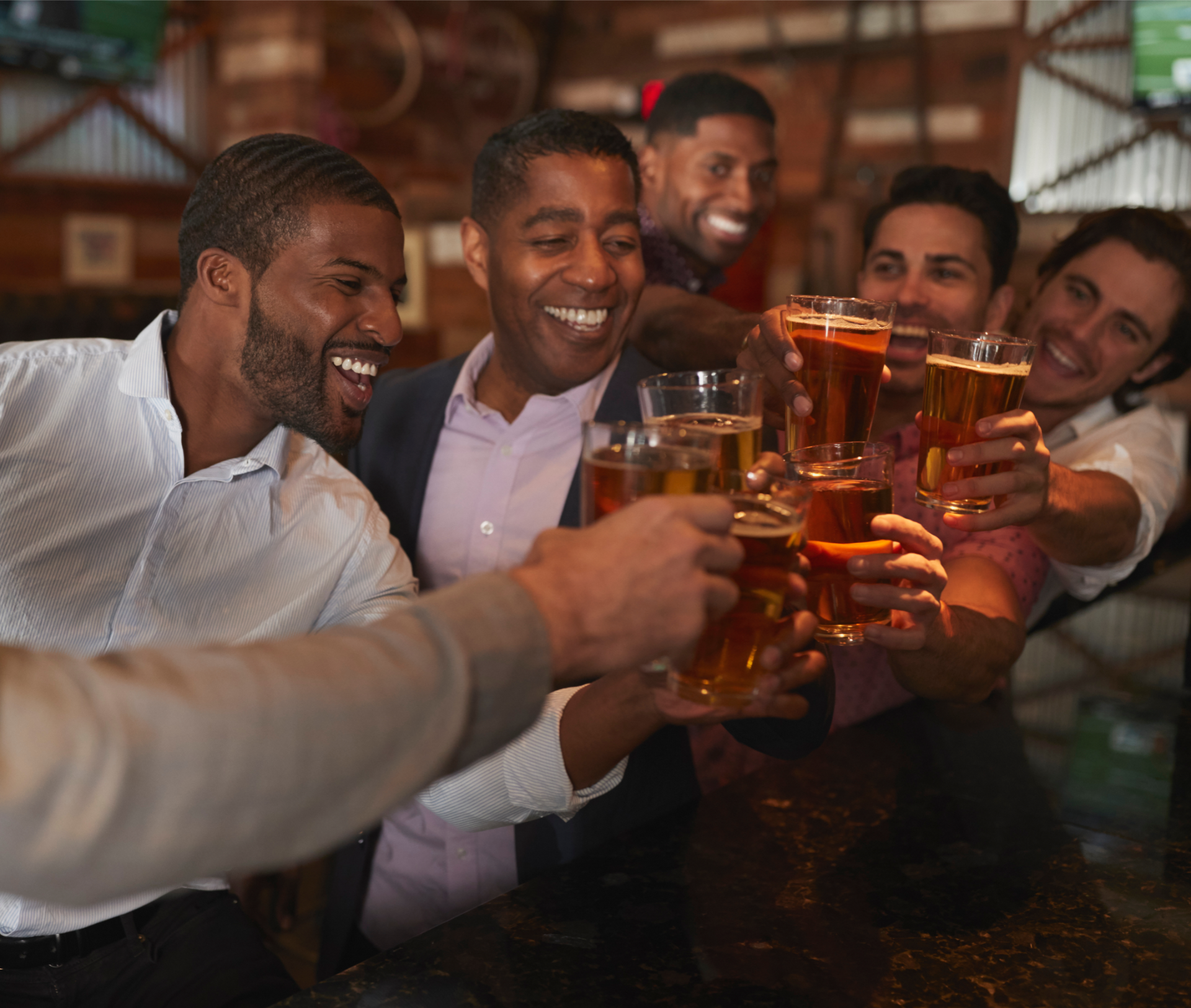 A group of people in a dimly lit bar toasting with glasses of beer, smiling and interacting with one another.