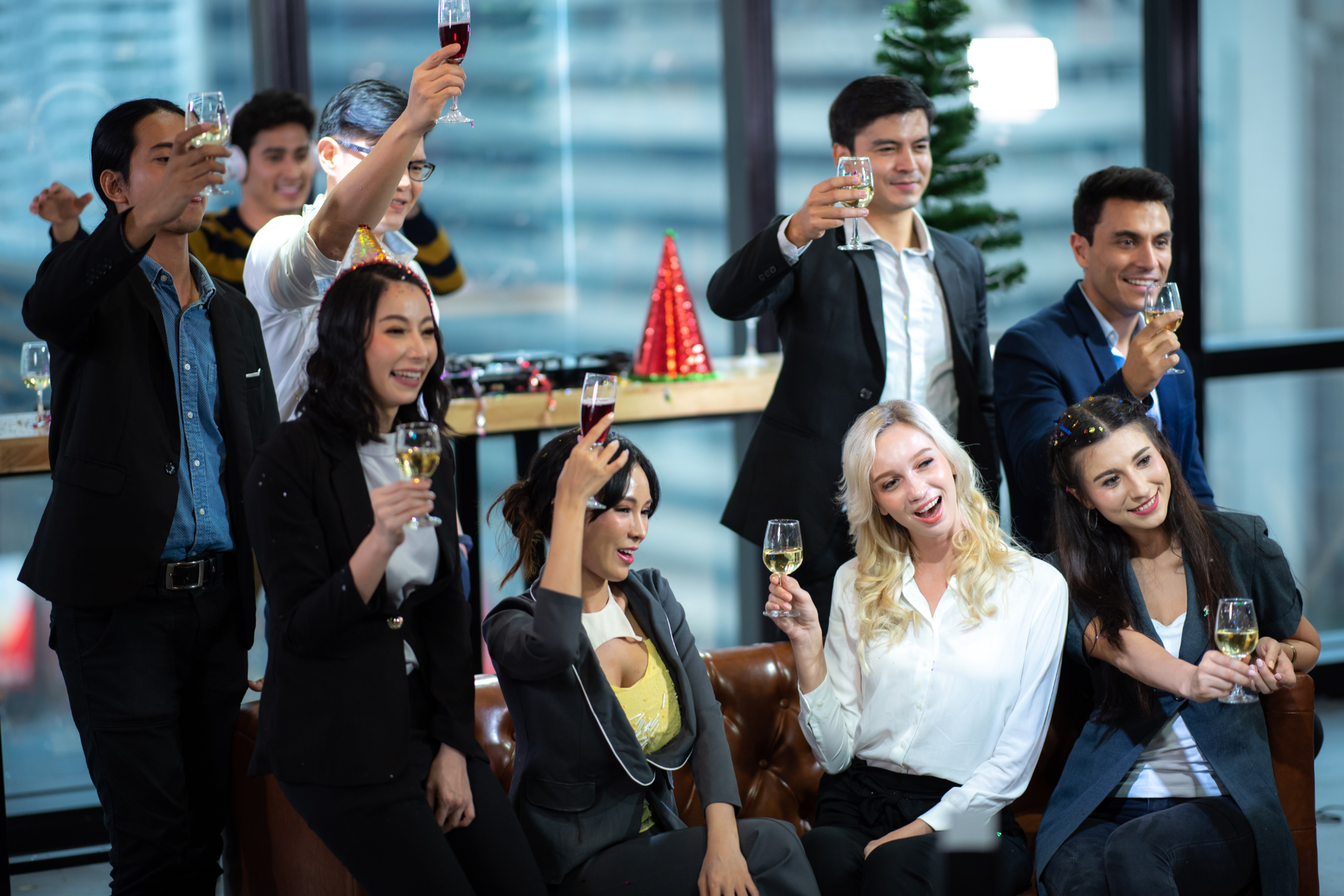A group of colleagues in professional attire celebrating and toasting with wine glasses in a modern office space.