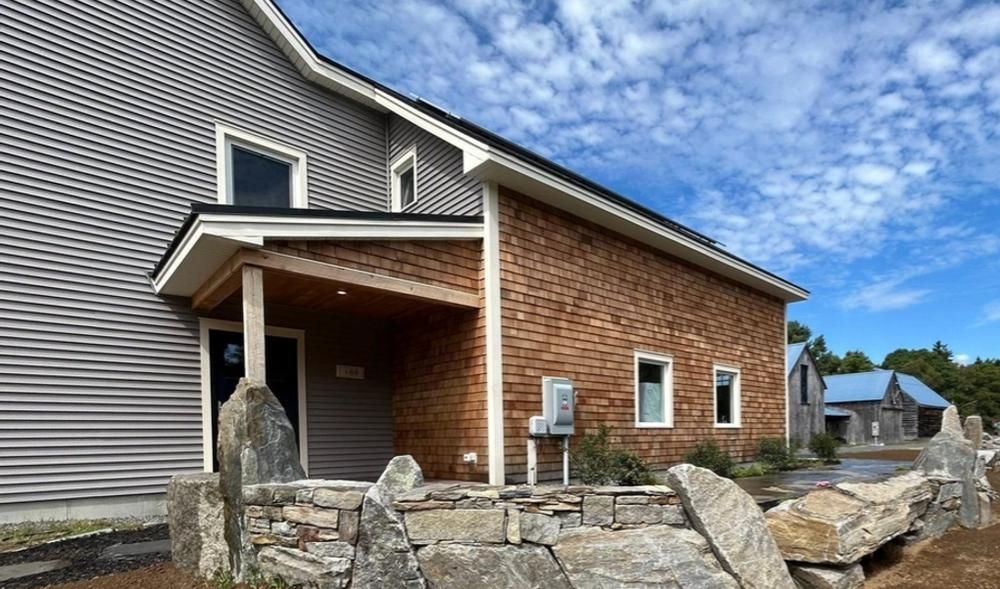 Brick-and-siding house exterior with a small covered porch and stone retaining wall under a blue sky