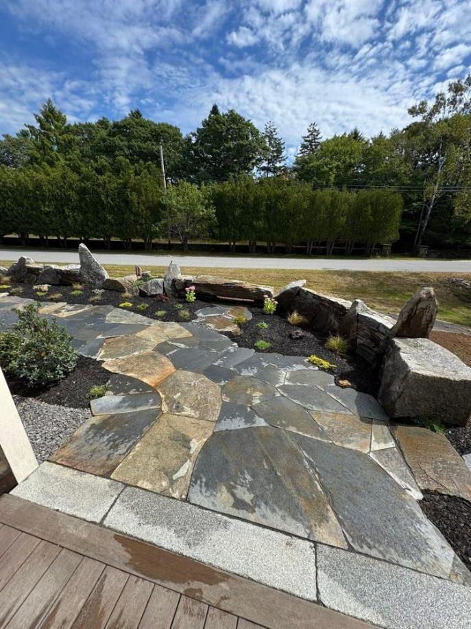 Stone patio and curved rock wall in a landscaped garden under a blue sky.