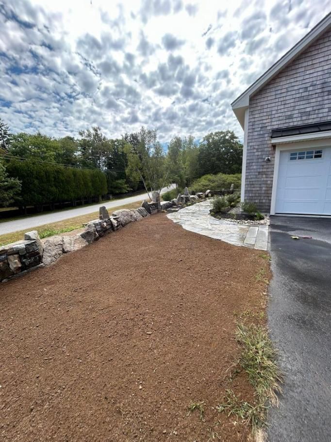 Freshly landscaped front yard with brown mulch, stone border, and a driveway beside a garage.