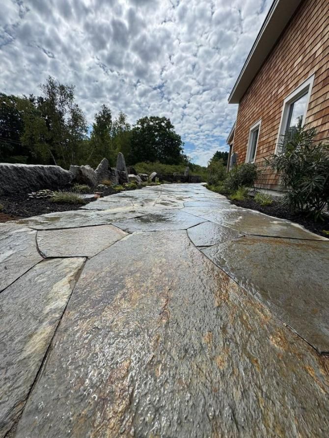 Stone walkway beside a brick house, with wet textured paving and a cloudy sky overhead
