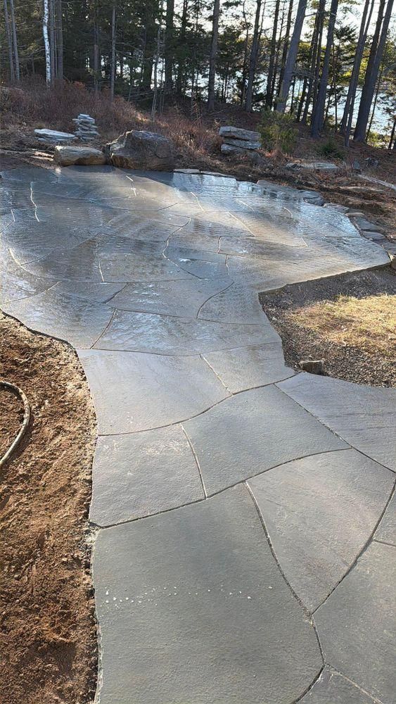 Cracked concrete patio curving through a yard with trees and mulch in the background