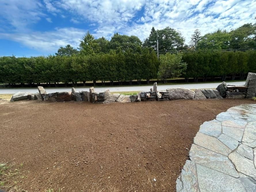 Landscaped park path with gravel, stone edging, and trees under a partly cloudy sky