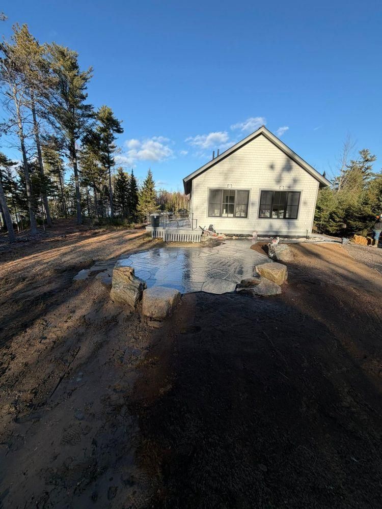 House with muddy driveway and large puddle reflecting the blue sky, surrounded by trees.