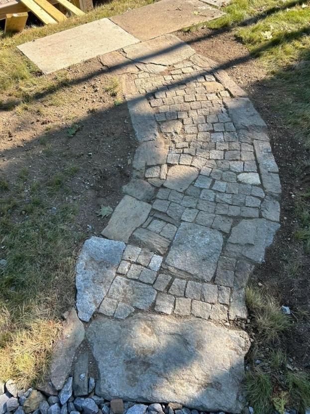 Broken stone walkway curving through grass in bright sunlight