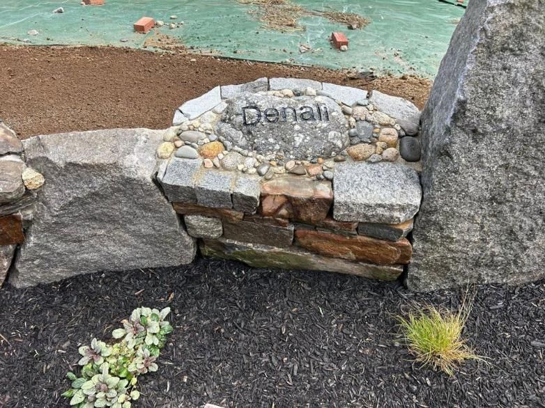 Small stone sign reading “Denali” in a landscaped garden bed with rocks and mulch