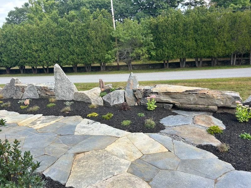 Rock garden with stacked stones and slate paving beside a tree-lined path