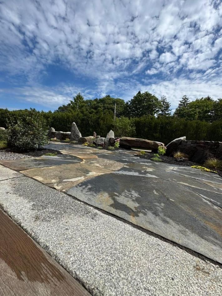 Stone patio and gravel path in a landscaped garden under a partly cloudy blue sky.