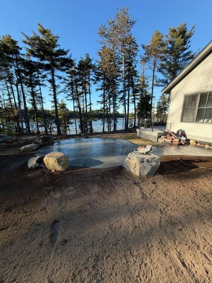 Winter lakeside patio with stone fire pit, trees, and a house in the background
