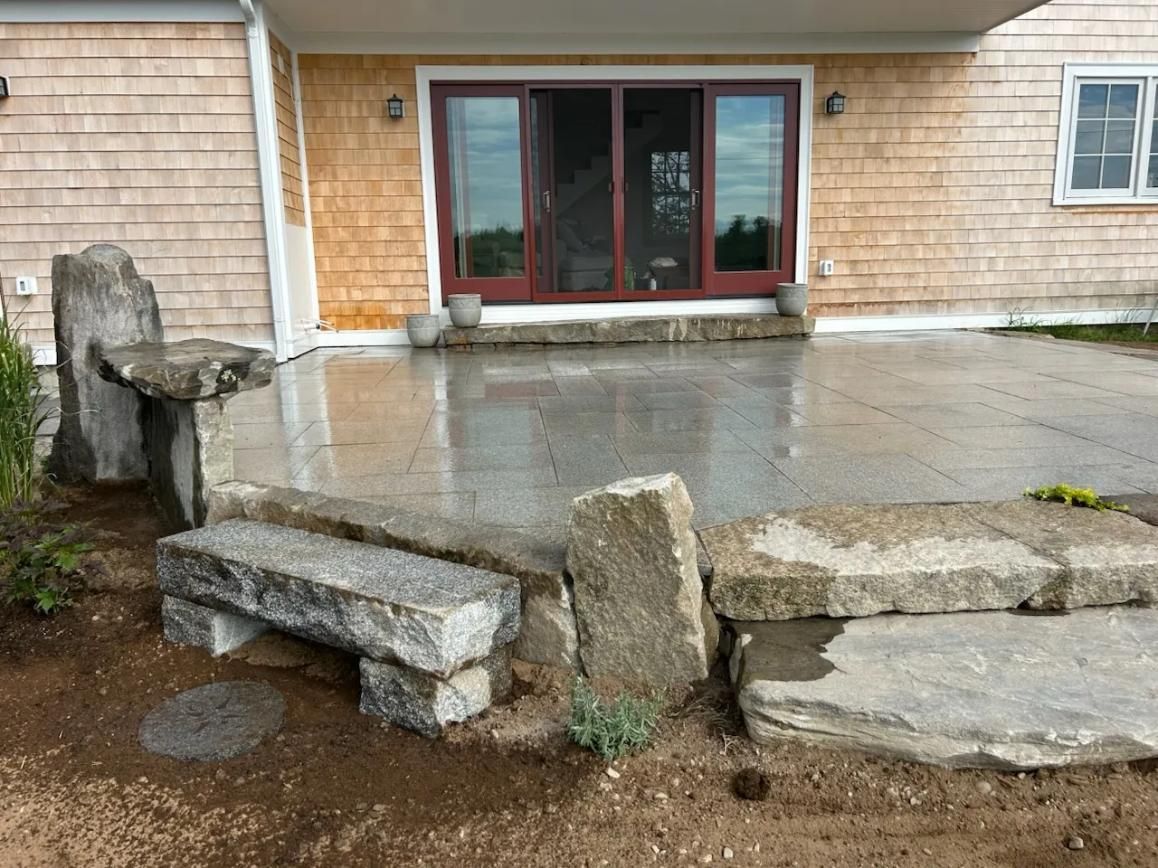 Wet concrete patio with broken stone steps and a sliding glass door on a house exterior