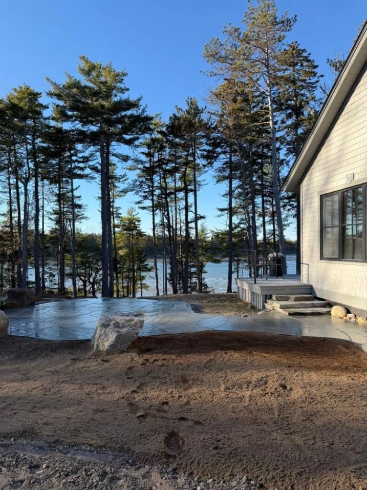 Cabin deck with icy yard, tall pine trees, and a bright blue sky beyond the lake