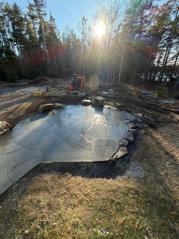 Sunlit backyard pond with partially frozen water, rocks, and a chair by the treeline