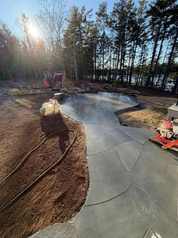 Freshly poured curved concrete path under construction beside trees and an excavator at sunset