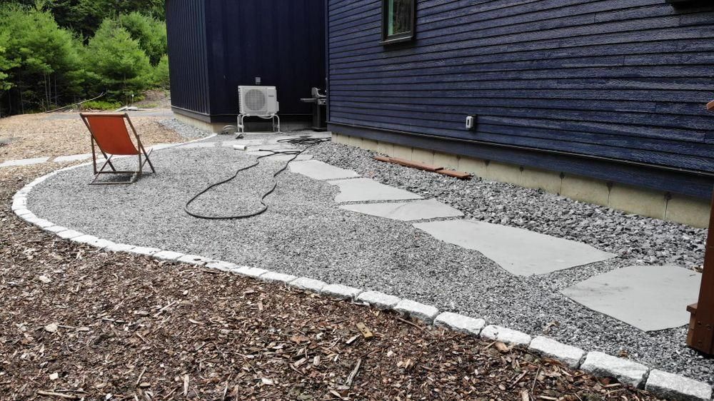 Gravel path beside a dark blue house, with white stepping stones and a red chair in the yard