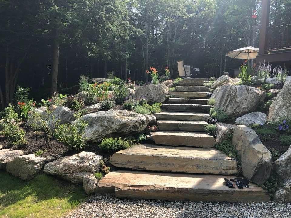 Stone steps leading through a landscaped rock garden with greenery and trees beyond.