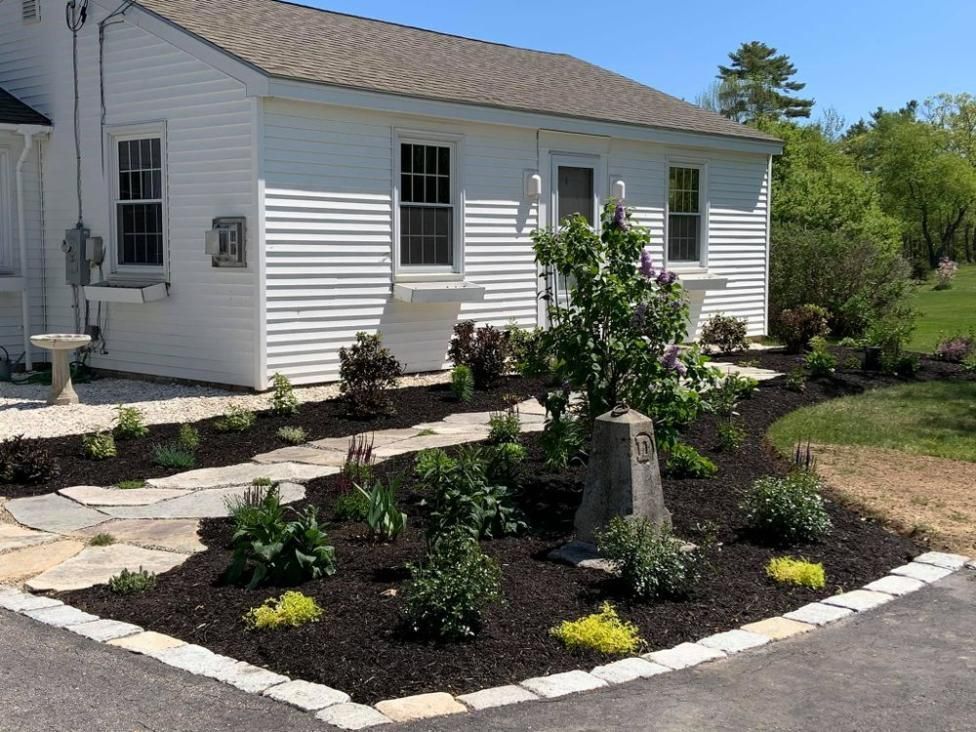White house with a curved flower bed and stone walkway in a landscaped yard
